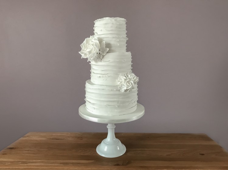 White wedding cake with ruffles and roses